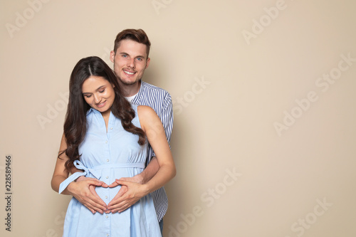 Young husband and his pregnant wife showing heart with hands on color background. Space for text © New Africa