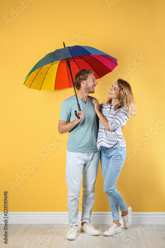 Couple with rainbow umbrella near color wall