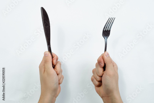 Hands are holding cutlery. Top view of a hand with a knife and a hand with a fork on a gray, bright background. Food and restaurant concept. Serving dishes, lunch, waiting for food. © Sebastian