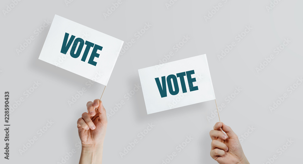 Hands raise the white flags with the word VOTE up. The concept of voting, making choices. Presidential and parliamentary elections. Calling for voting, democracy. Hands raise the white flags with the word VOTE up. The concept of voting, making choices. Presidential and parliamentary elections. Calling for voting, democracy.