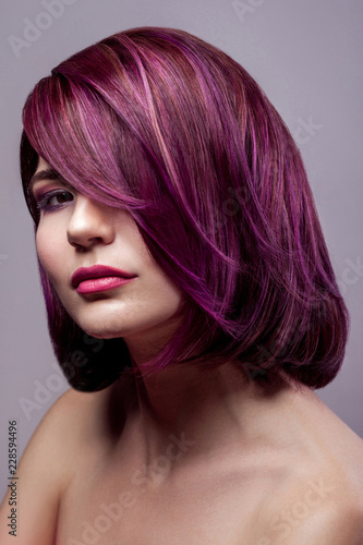 Portrait of beautiful fashion model woman with short purple colored hairstyle and makeup looking at camera. indoor studio shot, isolated on gray background.