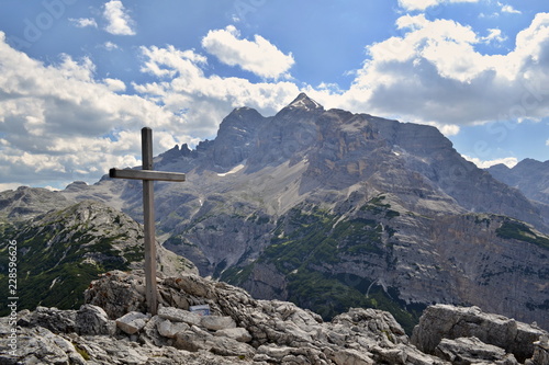 Wooden cross on a mountain peak with mountains under blue sky and white clouds in the background