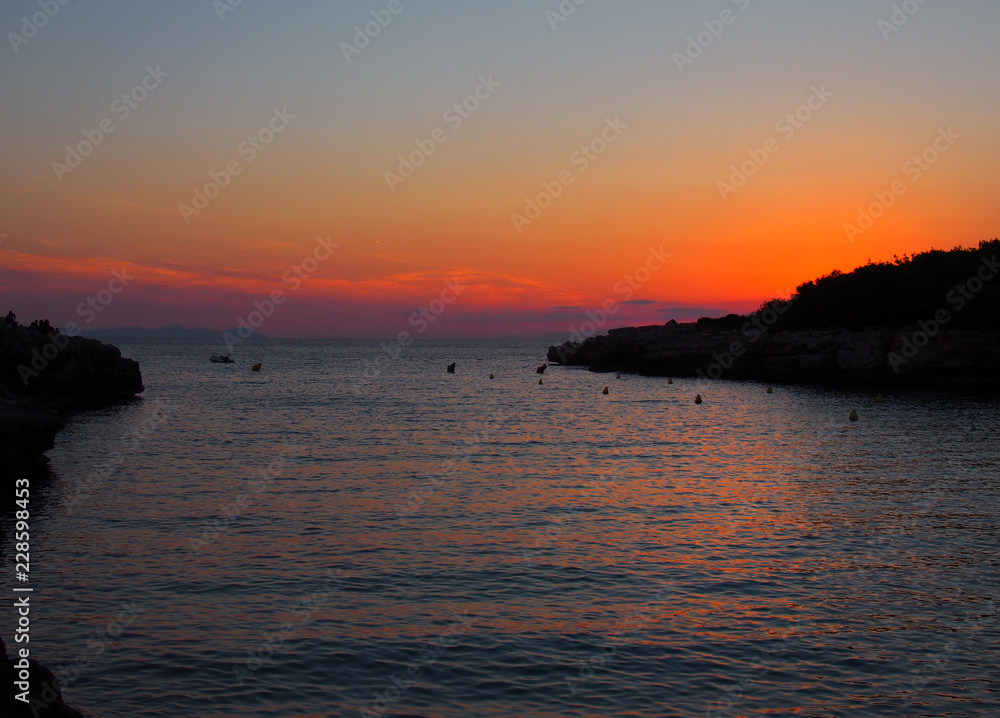 glowing evening twilight after sunset in the cala santandria bay in ciutadela menorca with a beautiful orange sky reflected in a dark sea with the land in silhouette