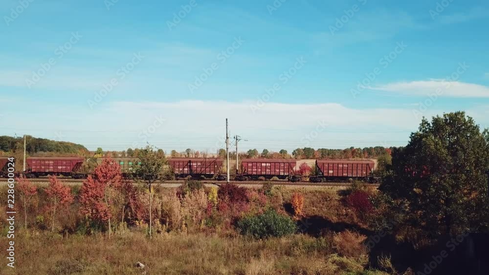 carriages of freight train are passing by rail in the field on the background of buildings of countryside in the summer. carriages of freight train are passing by rail in the field on the background of buildings of countryside in the summer.