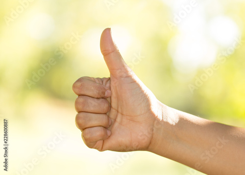 Woman hand doing sign with thumb up on nature background