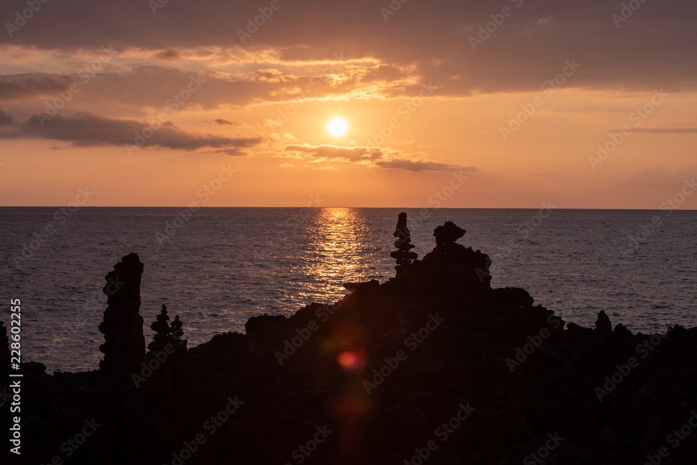 Tall rock formations with sunset over the Pacific ocean in the background