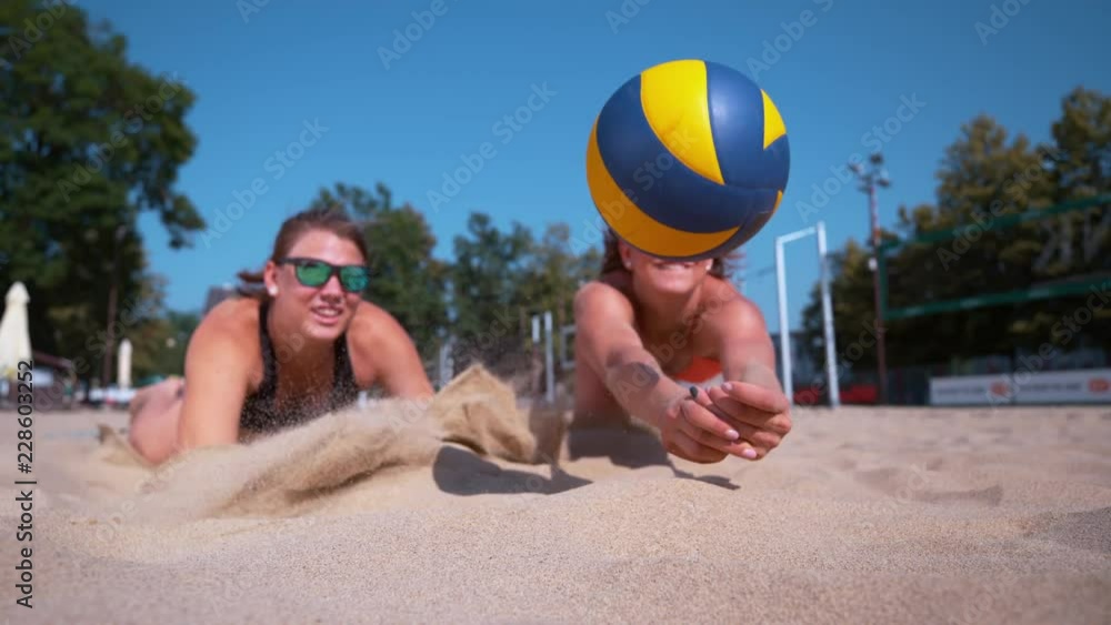 SLOW MOTION, CLOSE UP, DOF Female teammates both dive for the ball during a beach volleyball