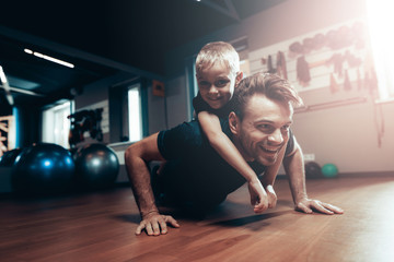 Man Is Doing Push Ups In Gym With Son On A Back.