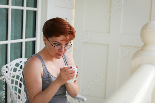 Woman relaxing on balcony holding cup of coffee or tea and amazedly looking at cup photo