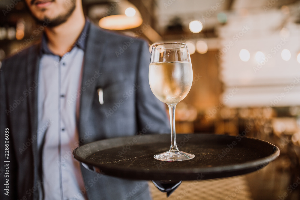 Φωτογραφία A young man carrying a tray with a glass of white wine