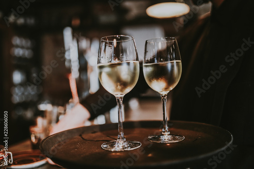 Two glasses of white wine glasses on the black tray, carried by a waiter. Restaurant, catering and celebraiton concept. photo