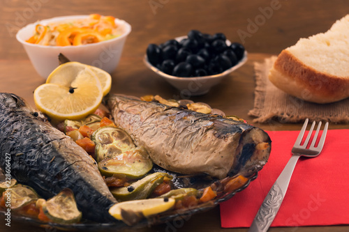 Fish baked with vegetables in the oven, laid on a plate with slices of lemon.