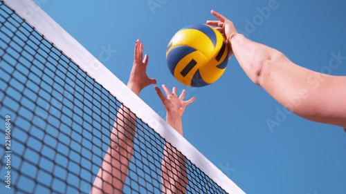 SLOW MOTION, CLOSE UP, LOW ANGLE: Unrecognizable young female' hands playing volleyball at the net. Offensive player spikes the ball and the opponent blocks it right above the net during a tournament. photo