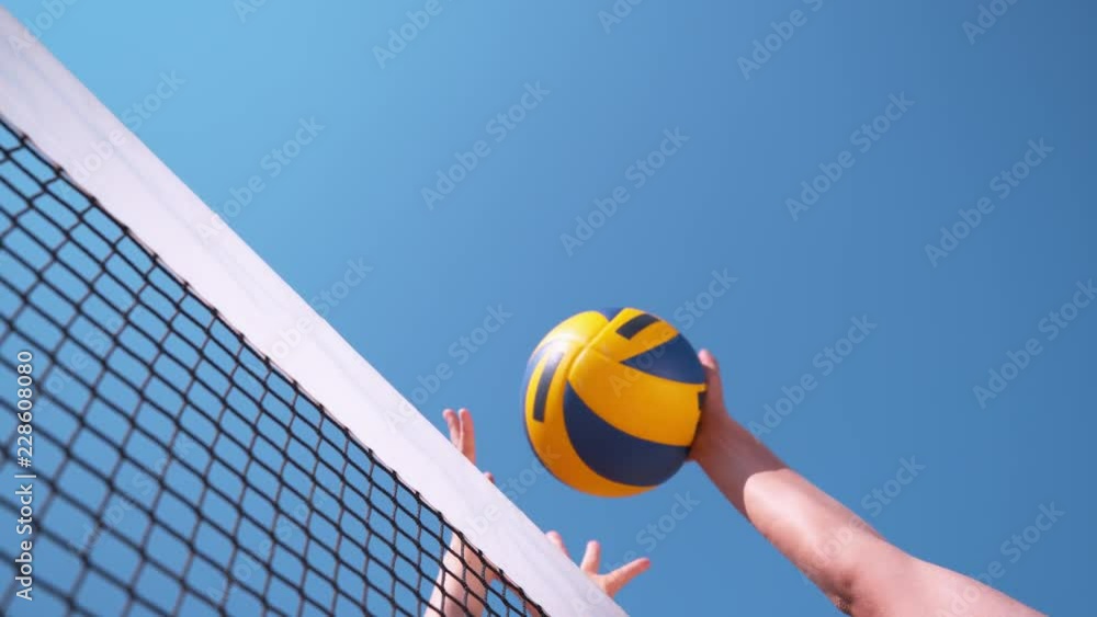 SLOW MOTION, CLOSE UP, LOW ANGLE: Unrecognizable volleyball player strikes the ball with her hand over the net and past the block and scores the point during a summer beach volleyball tournament.