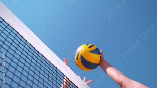 SLOW MOTION, CLOSE UP, LOW ANGLE: Unrecognizable volleyball player strikes the ball with her hand over the net and past the block and scores the point during a summer beach volleyball tournament. photo