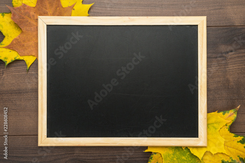 clean blackboard on wooden background with autumn leaves