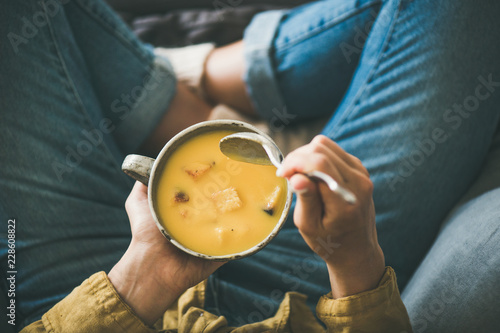 Flat-lay of female in yellow shirt sitting keeping mug of Fall warming pumpkin cream soup with croutons, top view. Autumn vegetarian, vegan, healthy comfort food eating concept