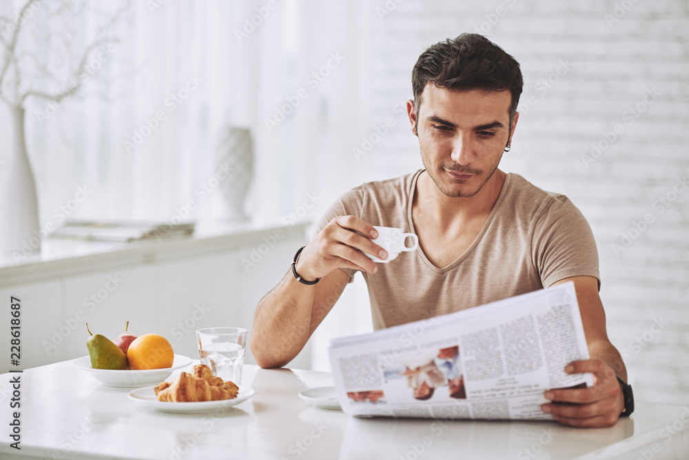 Young man enjoying breakfast and reading newspaper Young man enjoying breakfast and reading newspaper