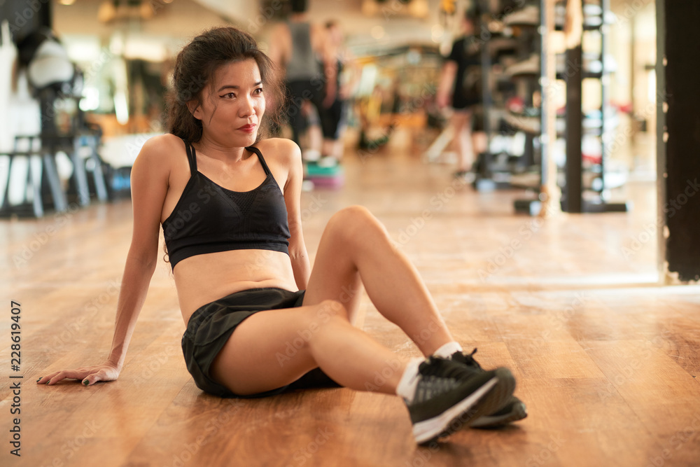 Smiling pretty fit Vietnamese woman resting on gym floor after training