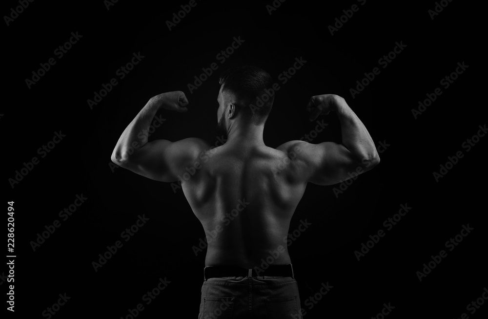 Bodybuilder black and white portrait. Muscular man stands back and shows biceps. Bodybuilder black and white portrait. Muscular man stands back and shows biceps.