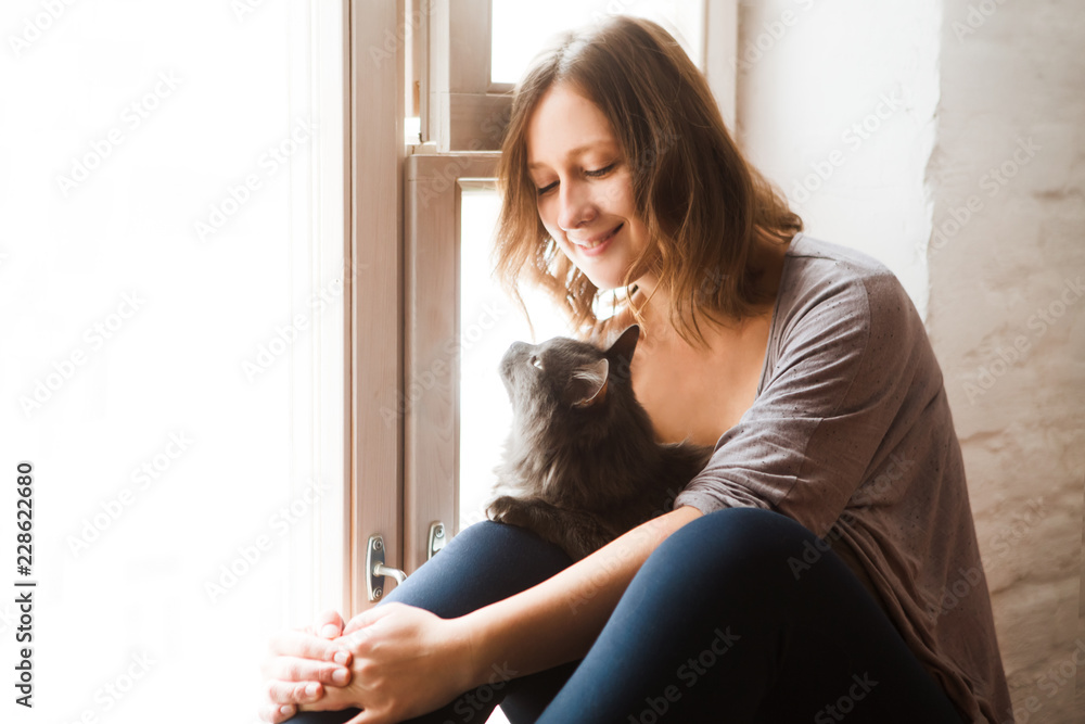 Young woman playing with cat about a window in home. Young woman playing with cat about a window in home.