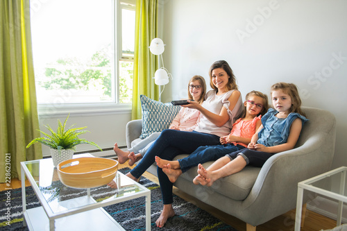 mother and daughters on sofa at home listening TV