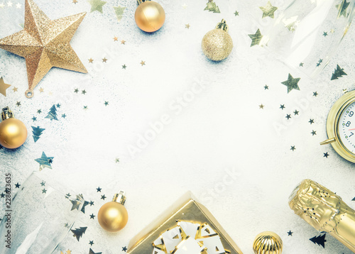 Christmas or New Year composition, frame, pink background with gold Christmas decorations, stars, snowflakes, balls, alarm clock, gift box and bottle of champagne, top view