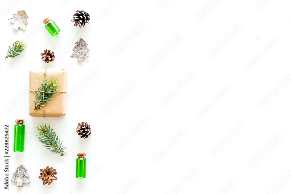 Composition with New Year gift wrapped in craft paper and decorted with pine sprout near pine sprigs, cones, spruce figure, fir oil on white background top view space for text