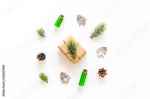 Composition with New Year gift wrapped in craft paper and decorted with pine sprout near pine sprigs, cones, spruce figure, fir oil on white background top view copy space