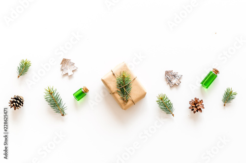 Composition with New Year gift wrapped in craft paper and decorted with pine sprout near pine sprigs, cones, spruce figure, fir oil on white background top view copy space photo