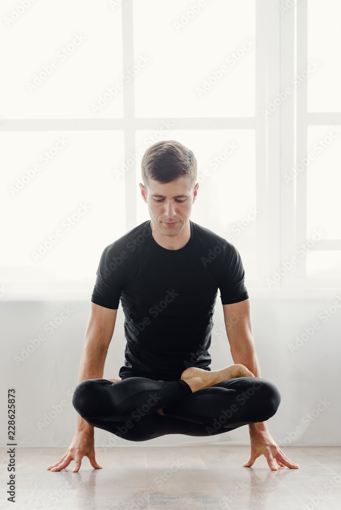 Fototapeta premium Young handsome man doing yoga exercises in yoga studio