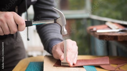 Fotografie Tanners hands at work with step punch, hammer and leather
