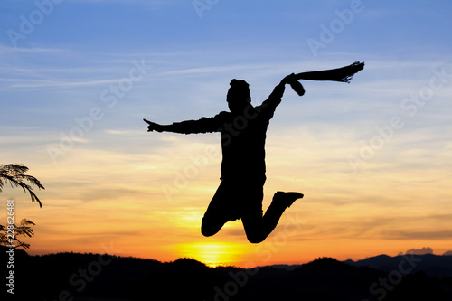 Silhouette of happy man jumping with raised hands at sunset or sunrise time © AungMyo