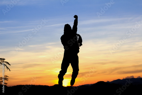 Silhouette of happy man jumping with raised hands at sunset or sunrise time