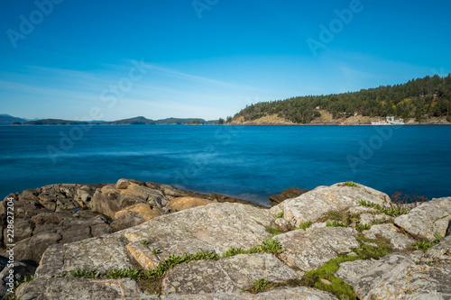 view of rocky coast under blue sunny sky with island on the far side