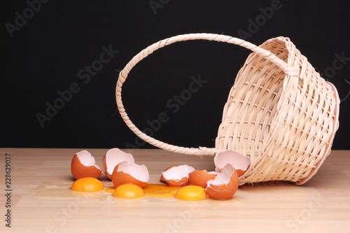Broken eggs next to an overturned wicker basket.  The risk of having alll eggs in one single basket. (Shallow depth of field) photo