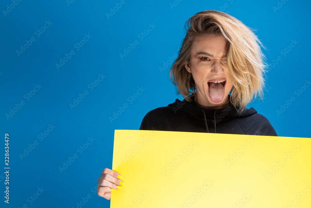 Funny dark blonde pulling hertongue out while holding an advertising cardboard and maing funny faces. Copy space available for ads Funny dark blonde pulling hertongue out while holding an advertising cardboard and maing funny faces. Copy space available for ads