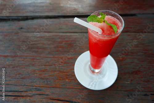 Watermelon smoothie in tall glass with mint leave and white straw on wooden table ,top view