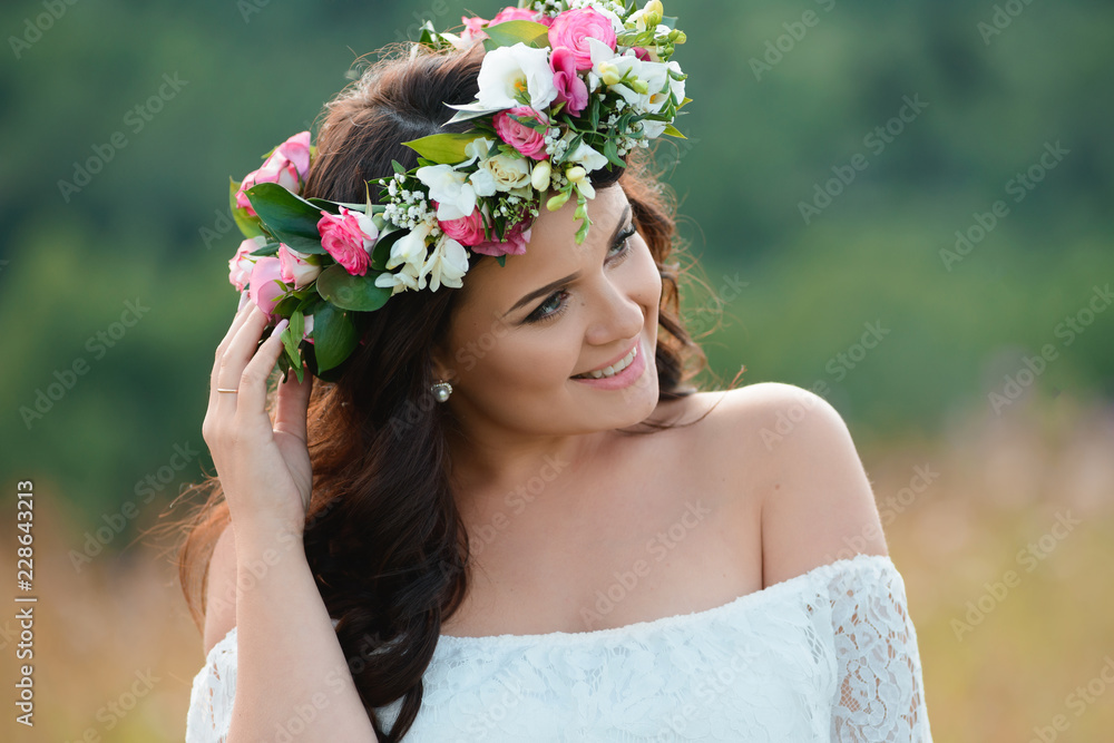 Smiling brunette girl with a wreath of flowers. Young woman with long hair in a white lace dress. Close-up female portrait Smiling brunette girl with a wreath of flowers. Young woman with long hair in a white lace dress. Close-up female portrait