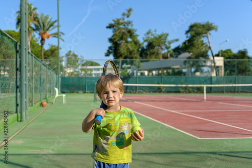 little boy with a tennis racket and ball on the court