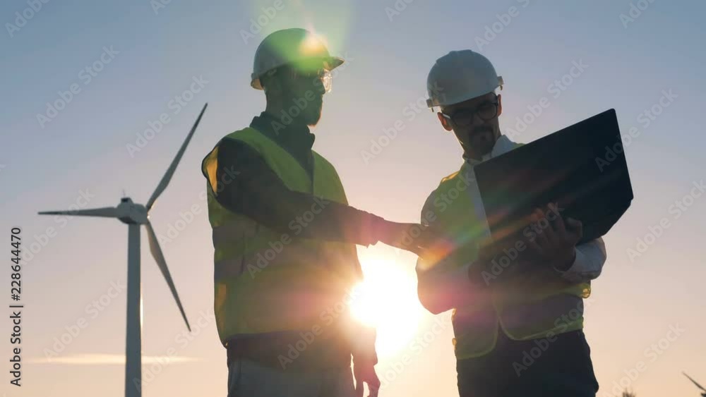 Renewable electririty, green energy concept. People working together near windmills.
