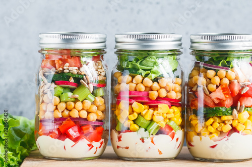 Three glass jars with layering various vegan salads for healthy lunch. The concept of fitness and vegetarian food.