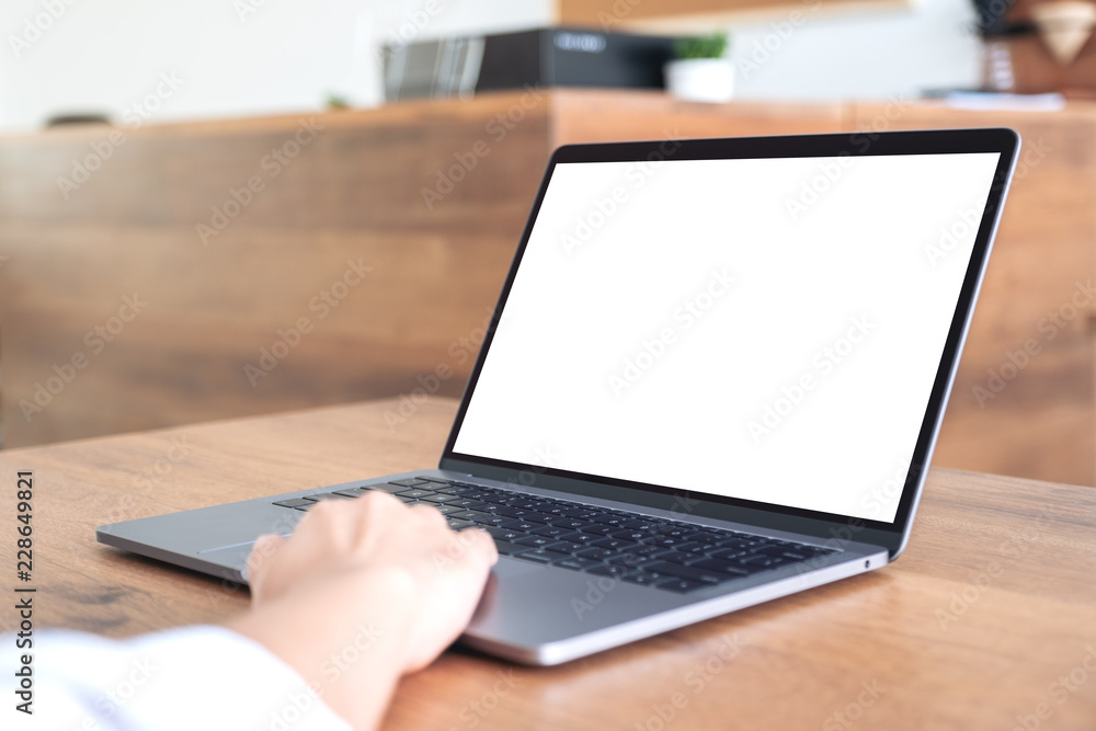 Mockup image of hand using and typing at laptop with blank white desktop screen on wooden table in office Mockup image of hand using and typing at laptop with blank white desktop screen on wooden table in office
