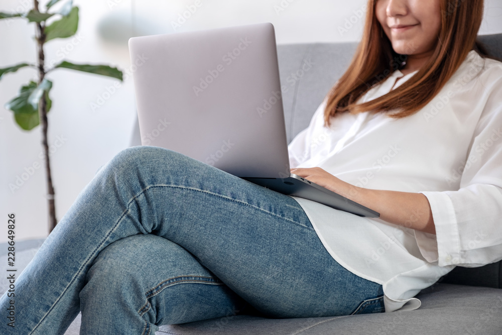 Closeup image of an asian woman using and typing on laptop keyboard while sitting on sofa with feeling relaxed Closeup image of an asian woman using and typing on laptop keyboard while sitting on sofa with feeling relaxed