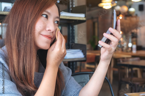 Closeup image of an asian woman looking in a mirror while putting on makeup