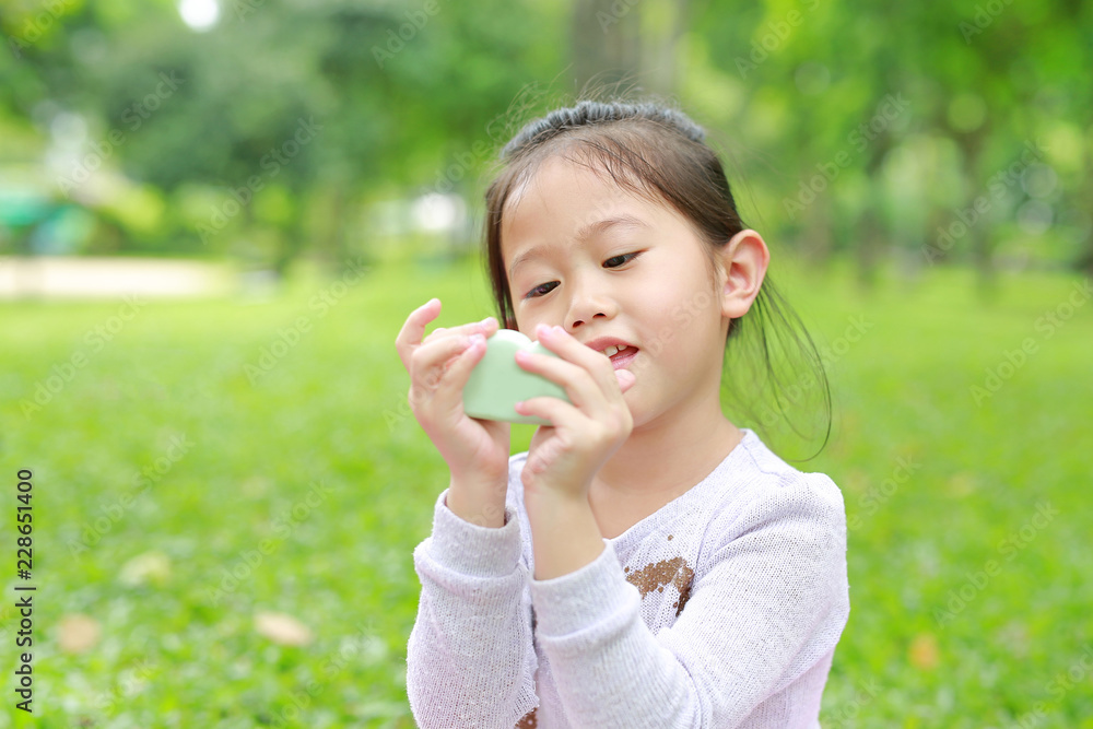 Cute little Asian child girl showing some food in her hands at green grass garden. Cute little Asian child girl showing some food in her hands at green grass garden.