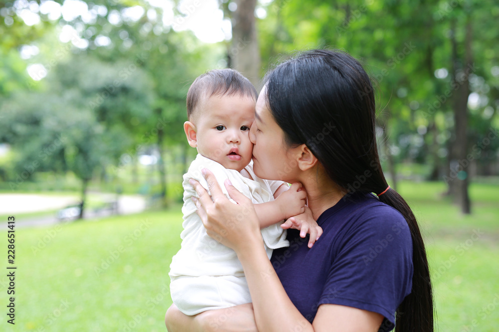 Asian mother carrying and kissing her infant baby boy in the green garden. Asian mother carrying and kissing her infant baby boy in the green garden.