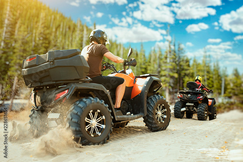 Two quad bike riders in helmets travels in forest