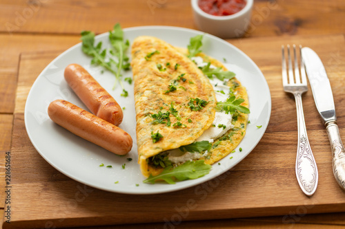 Omelette with herbs, soft cheese, grilled sausages and tomato sauce. Delicious breakfast