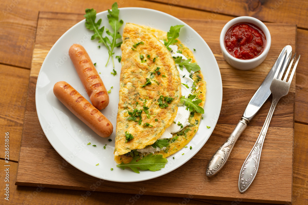 Omelette with herbs, soft cheese, grilled sausages and tomato sauce. Delicious breakfast Omelette with herbs, soft cheese, grilled sausages and tomato sauce. Delicious breakfast